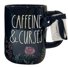 Load image into Gallery viewer, A glossy black ceramic mug with the words 'CAFFEINE &amp; CURSES' in white script, decorated with botanical illustrations including a pink rose and green leaves. A black ribbon bow with a white tag is tied to the handle.
