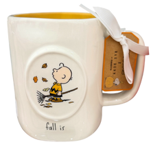 Load image into Gallery viewer, A white ceramic coffee mug featuring a circular inset of Charlie Brown sweeping leaves on a broomstick from the Peanuts comic strip. The mug has a yellow interior, a white ribbon bow tied to the handle, and a paper tag.
