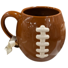 Load image into Gallery viewer, A brown ceramic football mug with a 3D football design, featuring a white laces detail and a small white ribbon bow on the handle, set against a plain white background.
