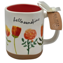 Load image into Gallery viewer, Mug with floral design and 'hello sunshine' text, featuring a tag on a white background that has a red inside and tan bottom.
