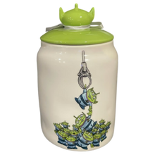 Load image into Gallery viewer, White canister that has an image of Toy Story aliens being pulled up by a claw machine and has a green lid with the back of an alien head as the handle.
