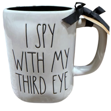 Load image into Gallery viewer, A white ceramic mug with the phrase 'I SPY WITH MY THIRD EYE' printed in black lettering. A black ribbon bow is tied to the handle, and a small beige tag is attached.
