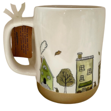Load image into Gallery viewer, A ceramic mug with a cream-colored upper body, a brown glazed base, and a whimsical hand-drawn illustration of houses, a tree, and a mouse. A brown paper hang tag is attached to the handle with a white ribbon.
