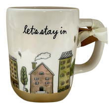 Load image into Gallery viewer, A white ceramic mug with a brown base and handle, featuring the phrase 'let's stay in' in black script above a hand-drawn illustration of apartment buildings, trees, and a cloud. A white ribbon bow is tied to the handle.
