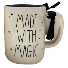 Load image into Gallery viewer, An off-white ceramic mug with a dark navy blue interior, featuring the text 'MADE WITH MAGIC' in a black hand-drawn font, decorated with small black stars. A black ribbon is tied to the handle.
