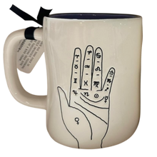 Load image into Gallery viewer, An off-white ceramic mug with a dark navy blue interior and rim, featuring a black line art illustration of a hand with zodiac and astrological symbols. A black ribbon and a paper tag are attached to the handle.
