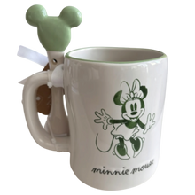 Load image into Gallery viewer, A white ceramic mug featuring a green Minnie Mouse graphic and the text 'minnie mouse' on the front, with a mint green Mickey-shaped spoon tucked into the side of the mug.
