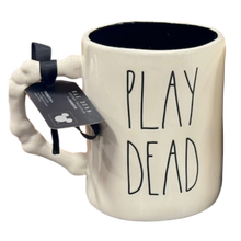 Load image into Gallery viewer, A ceramic mug shaped like a skeletal bones with a black ribbon tag, with the words 'PLAY DEAD' printed in black on the side. The mug is off-white with a black interior.
