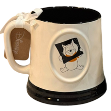 Load image into Gallery viewer, A ceramic Disney mug with a cream-colored exterior, black interior and base, featuring Winnie the Pooh holding a black square with a cat face shape cut out with an orange shirt on. A white ribbon bow is tied to the handle, and a Disney tag is attached.
