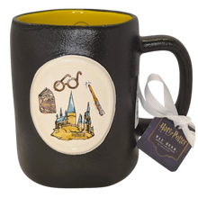 Load image into Gallery viewer, A black ceramic Harry Potter Mug with a yellow interior, featuring a circular white emblem on the front with illustrations of round glasses, a wand, a book, and Hogwarts castle. A white ribbon and a 'Harry Potter' tag are attached to the handle.
