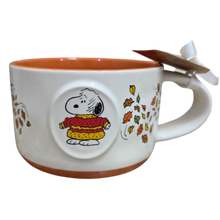Load image into Gallery viewer, A white ceramic Snoopy mug with an orange-brown interior and base, featuring a circular 3D Snoopy in a red and yellow sweater, surrounded by autumn leaves. A wooden tea bag rests on the handle.
