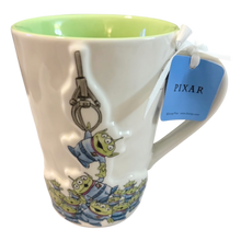 Load image into Gallery viewer, Mug with Pixar character design and tag on a white background with green interior showing green aliens being pulled up by a claw.
