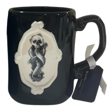 Load image into Gallery viewer, A glossy black ceramic mug featuring a raised white decorative plaque with a black-and-white snake and skull illustration. A hangtag is attached to the handle.
