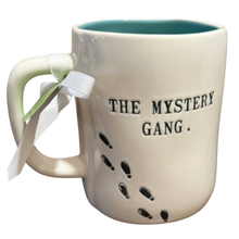 Load image into Gallery viewer, An off-white ceramic mug with a teal interior, featuring the text 'THE MYSTERY GANG.' and black footprint graphics on the side.
