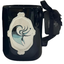 Load image into Gallery viewer, A glossy black ceramic mug with a white embossed crest featuring a stylized blue and black drawing of Zero from Nightmare Before Christmas. The handle is wrapped in a black ribbon with a branded tag attached.
